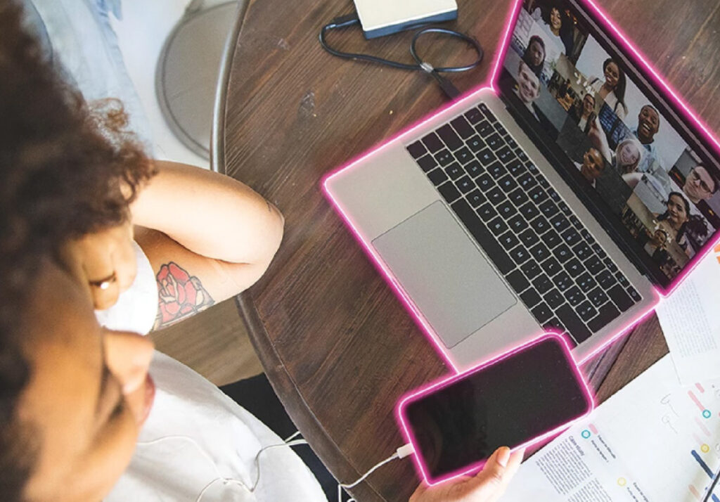 A woman working on a computer connected to a phone with papers showing data charts and graphs to provide your brand with sustained performance and growth as a part of YouTube channel management services.